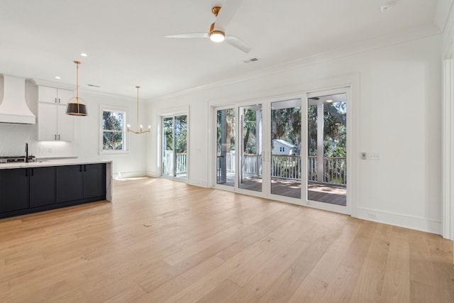 unfurnished living room with light wood-type flooring, baseboards, ornamental molding, and ceiling fan with notable chandelier