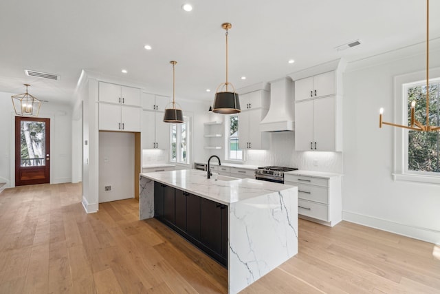 kitchen with tasteful backsplash, custom range hood, visible vents, light wood-style flooring, and gas range