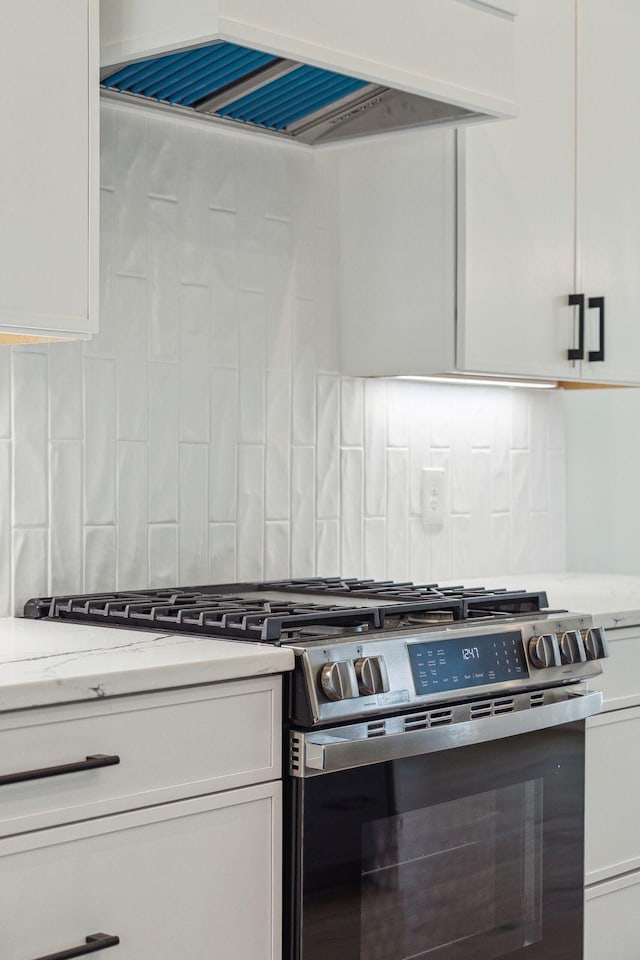 kitchen with stainless steel gas range oven, backsplash, custom exhaust hood, and white cabinets