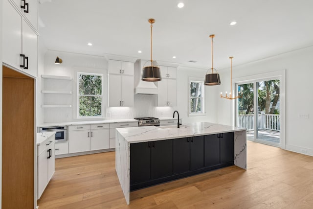 kitchen with a sink, white cabinets, appliances with stainless steel finishes, light wood-type flooring, and plenty of natural light