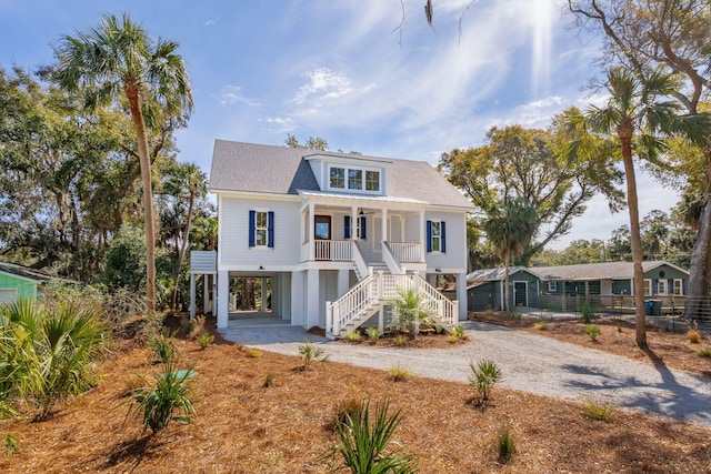 coastal home featuring covered porch, stairs, dirt driveway, and a carport