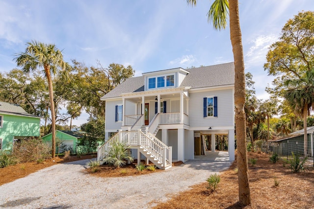 coastal inspired home featuring driveway, a shingled roof, stairs, a porch, and a carport