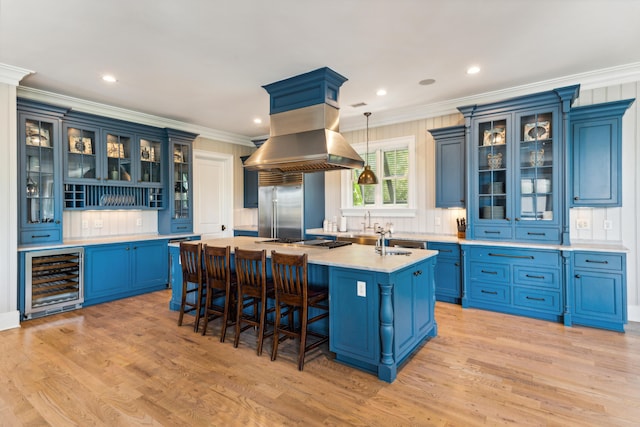 kitchen featuring appliances with stainless steel finishes, light countertops, beverage cooler, a center island with sink, and blue cabinets