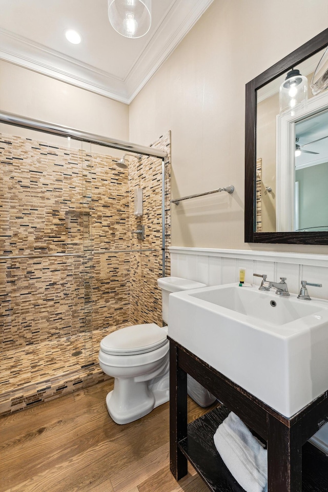 bathroom featuring crown molding, wood finished floors, toilet, a wainscoted wall, and a stall shower