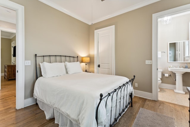 bedroom featuring crown molding, baseboards, wood finished floors, and connected bathroom