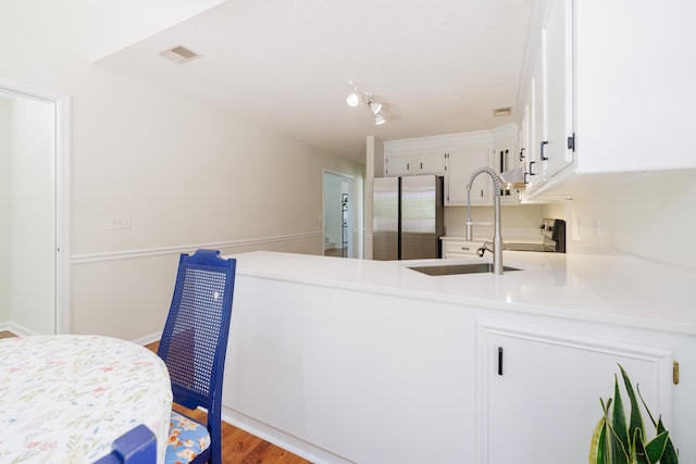 kitchen featuring visible vents, freestanding refrigerator, a peninsula, light countertops, and white cabinets