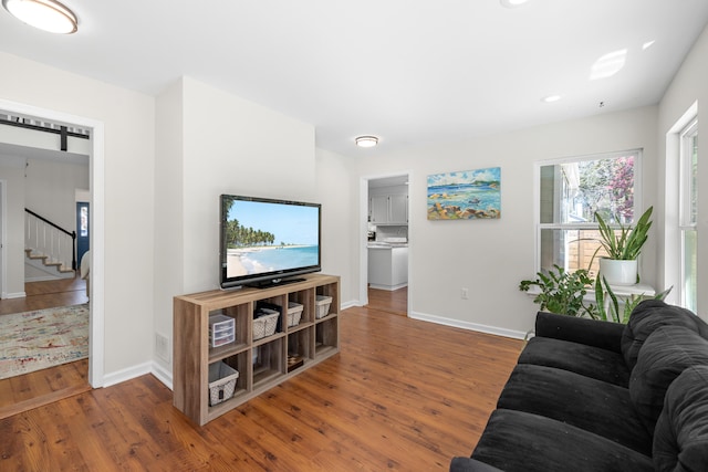 living room featuring baseboards, a barn door, wood finished floors, and stairway