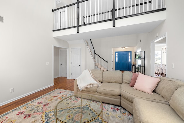 living area with visible vents, wood finished floors, stairway, baseboards, and a high ceiling