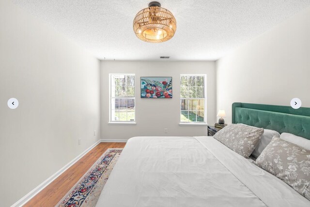 bedroom featuring visible vents, baseboards, a textured ceiling, and wood finished floors