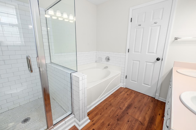 full bath with double vanity, a bath, a shower stall, wood finished floors, and a sink