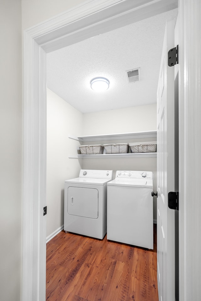 laundry area featuring visible vents, wood finished floors, and washing machine and clothes dryer