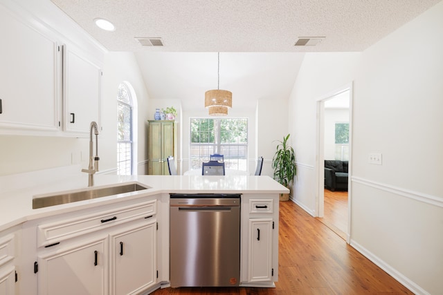 kitchen featuring visible vents, a peninsula, a sink, dishwasher, and vaulted ceiling