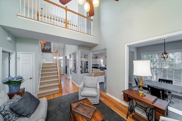living area with baseboards, stairway, a high ceiling, wood finished floors, and a ceiling fan