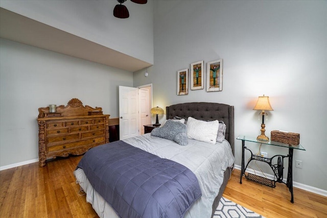 bedroom with baseboards, wood finished floors, and a towering ceiling