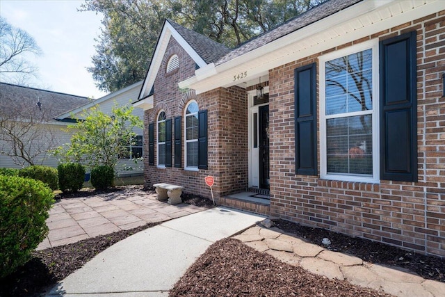entrance to property with brick siding and a shingled roof