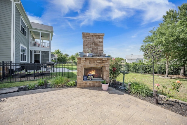 view of patio with an outdoor stone fireplace and a balcony
