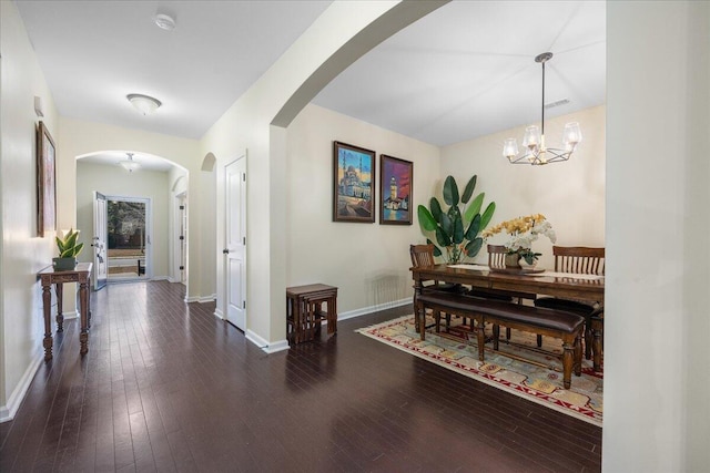 hallway with wood-type flooring, arched walkways, a chandelier, and baseboards