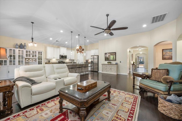 living room featuring lofted ceiling, ceiling fan, visible vents, and dark wood finished floors