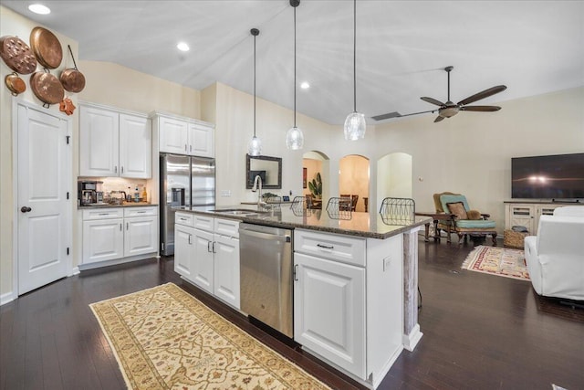 kitchen with arched walkways, stainless steel appliances, a kitchen island with sink, a sink, and white cabinetry