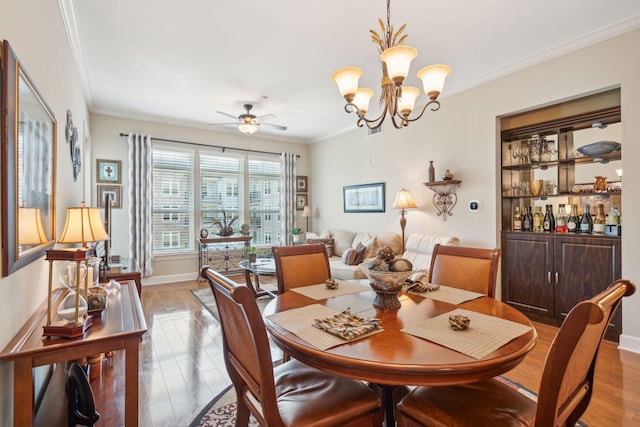 dining space with baseboards, crown molding, light wood finished floors, and ceiling fan with notable chandelier