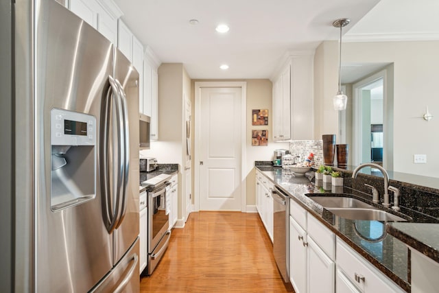 kitchen featuring light wood-style flooring, a sink, white cabinets, hanging light fixtures, and appliances with stainless steel finishes