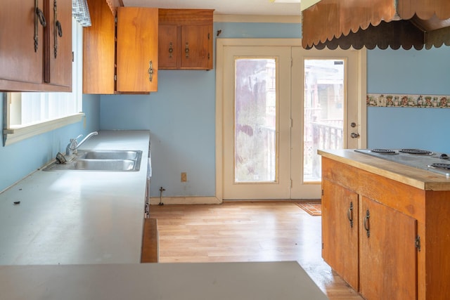 kitchen with brown cabinets, light countertops, light wood-style floors, a sink, and stovetop