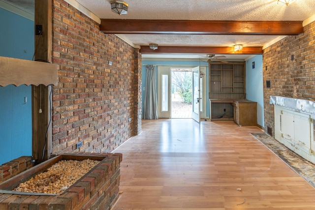 interior space featuring a textured ceiling, brick wall, beamed ceiling, and light wood-style flooring