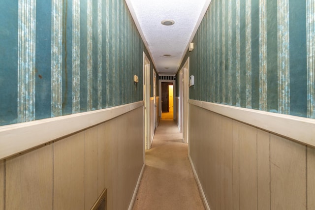 hallway with a wainscoted wall, a textured ceiling, visible vents, and light colored carpet