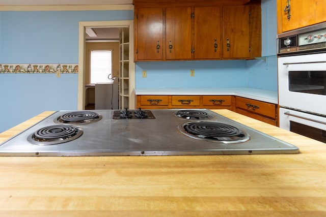 kitchen featuring brown cabinets, black electric cooktop, light countertops, and white double oven