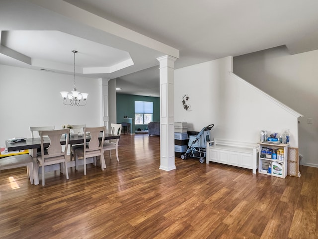 dining space featuring decorative columns, an inviting chandelier, a tray ceiling, and dark hardwood / wood-style floors