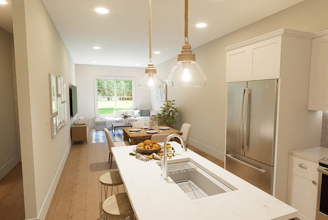 kitchen with hanging light fixtures, a sink, freestanding refrigerator, and white cabinetry