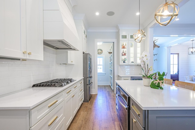 kitchen with white cabinets, appliances with stainless steel finishes, custom range hood, and ornamental molding