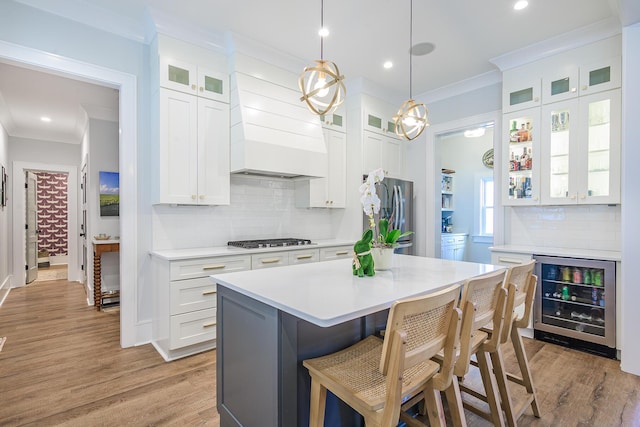 kitchen with a breakfast bar area, ornamental molding, light countertops, wine cooler, and appliances with stainless steel finishes