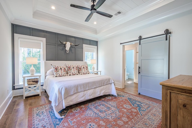 bedroom featuring a tray ceiling, a barn door, and multiple windows