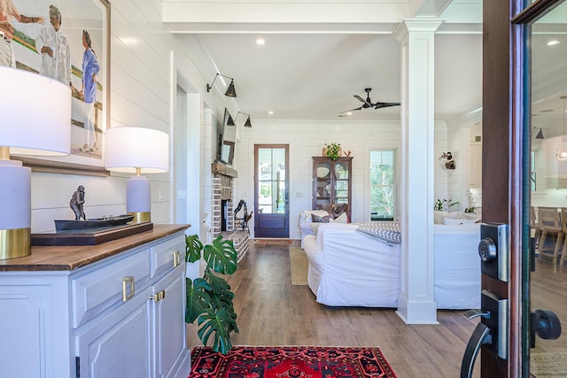 interior space with crown molding, decorative columns, a stone fireplace, wood finished floors, and a ceiling fan