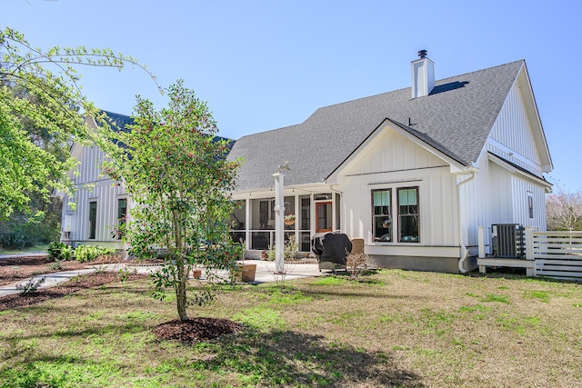 rear view of house featuring a shingled roof, cooling unit, a chimney, a yard, and a sunroom