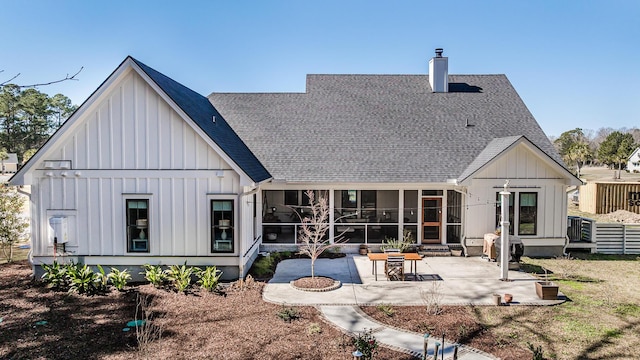 rear view of house with a patio, a sunroom, board and batten siding, a shingled roof, and a chimney