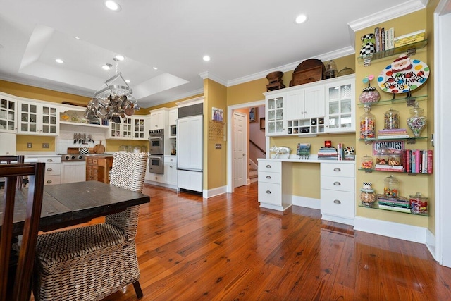 kitchen featuring dark hardwood / wood-style flooring, appliances with stainless steel finishes, a tray ceiling, white cabinetry, and built in desk