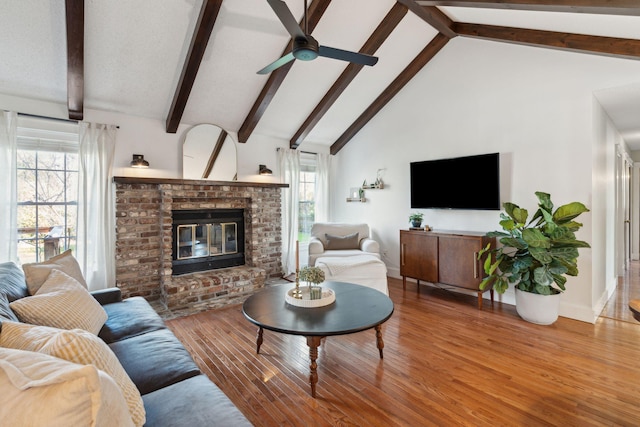 living area featuring a brick fireplace, beamed ceiling, wood finished floors, high vaulted ceiling, and a ceiling fan