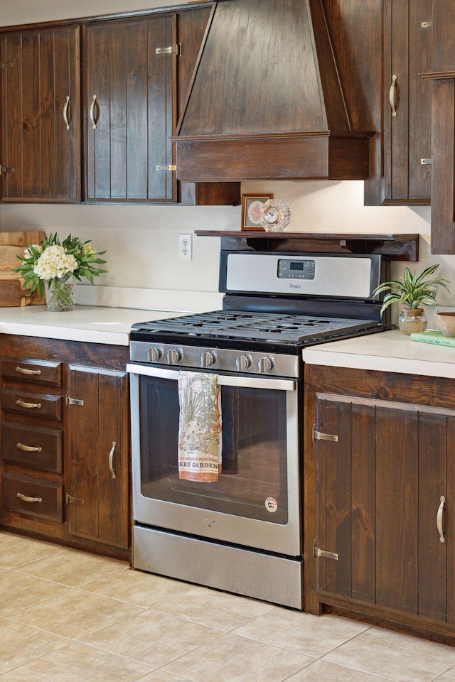 kitchen featuring stainless steel gas range oven, dark brown cabinetry, light countertops, and custom range hood