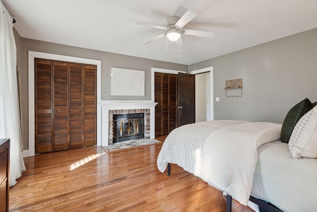 bedroom with a glass covered fireplace, ceiling fan, two closets, and light wood-style floors