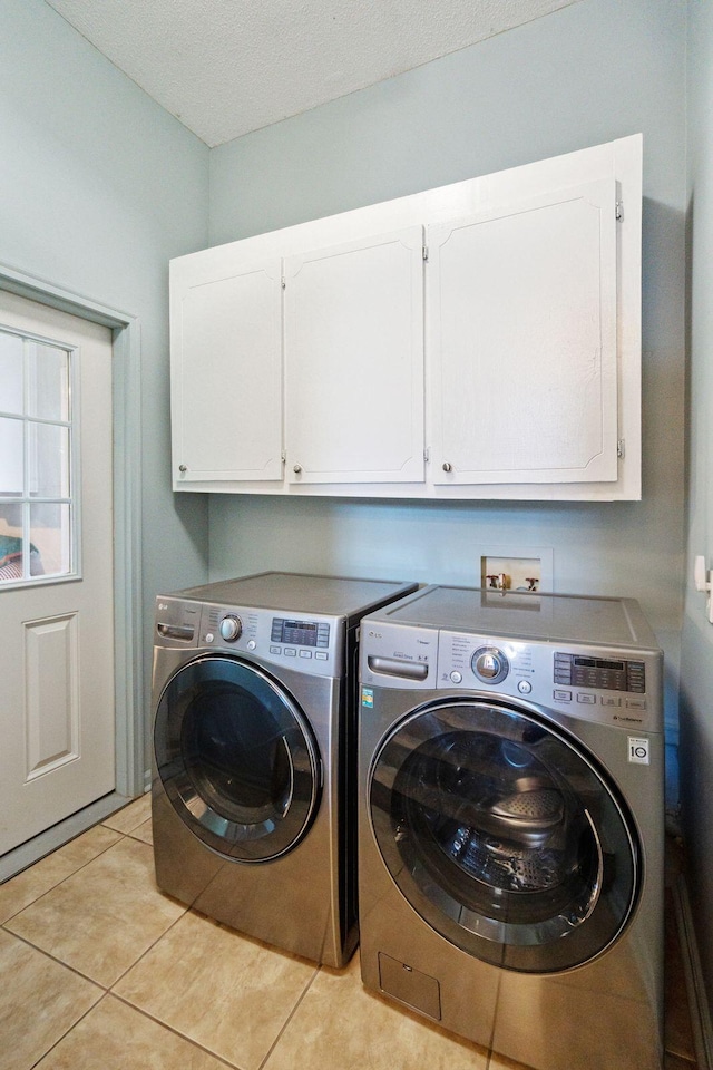 washroom with cabinet space, a textured ceiling, light tile patterned flooring, and washer and clothes dryer