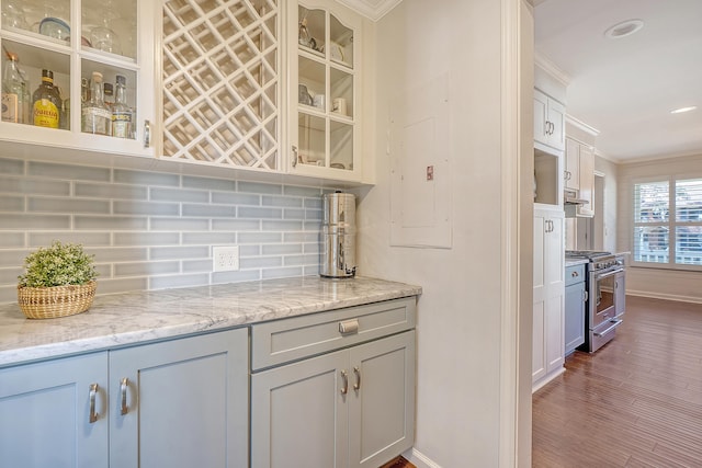 kitchen with backsplash, ornamental molding, glass insert cabinets, high end stove, and electric panel