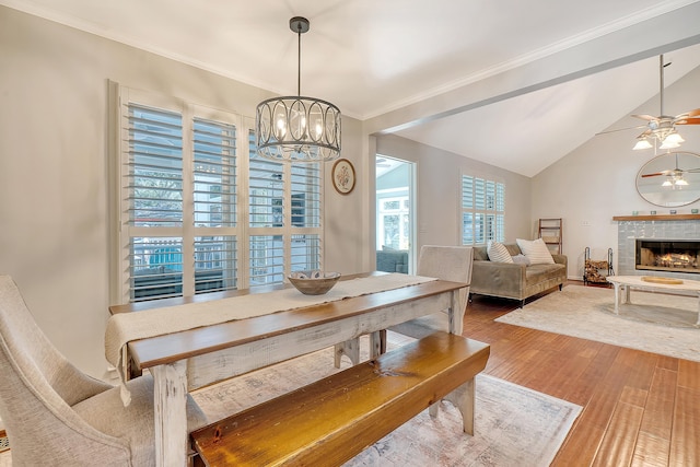 dining space featuring crown molding, vaulted ceiling, wood finished floors, a tile fireplace, and ceiling fan with notable chandelier