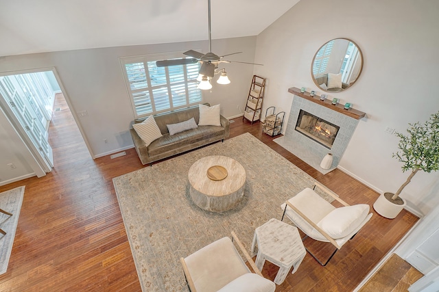 living area featuring visible vents, a tiled fireplace, a ceiling fan, wood finished floors, and baseboards