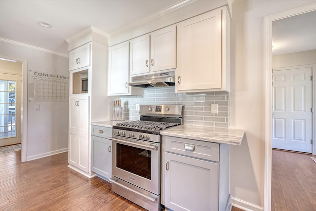 kitchen featuring stainless steel gas stove, light wood finished floors, tasteful backsplash, baseboards, and under cabinet range hood