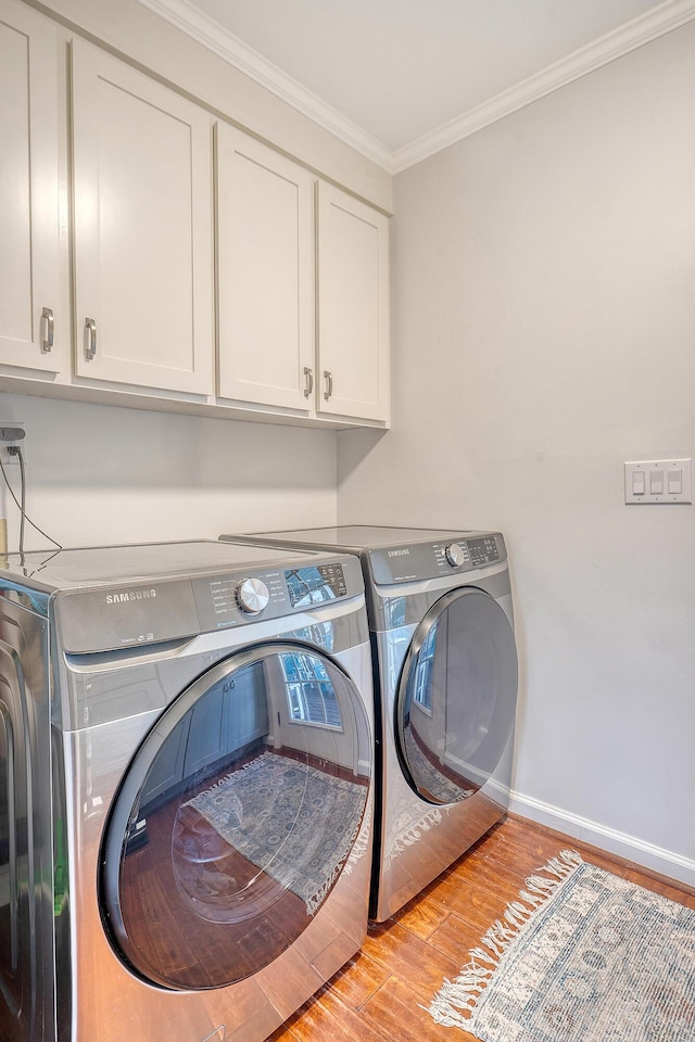 laundry room with wood finished floors, baseboards, cabinet space, washer and clothes dryer, and crown molding