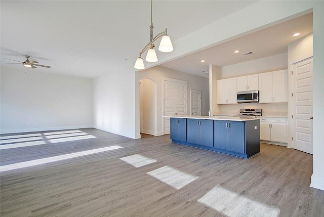 kitchen featuring white cabinetry, a center island with sink, stainless steel appliances, hanging light fixtures, and light hardwood / wood-style flooring