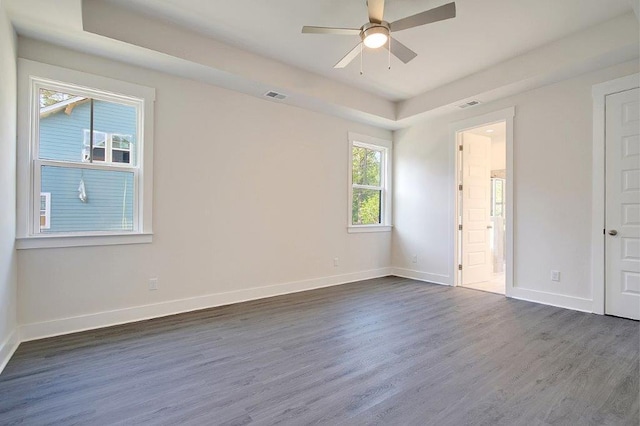 unfurnished bedroom featuring ensuite bathroom, dark hardwood / wood-style flooring, ceiling fan, and a raised ceiling