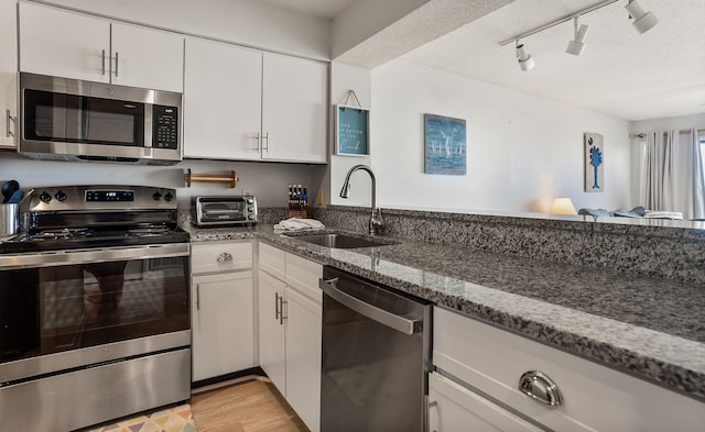 kitchen featuring appliances with stainless steel finishes, sink, white cabinetry, rail lighting, and dark stone countertops